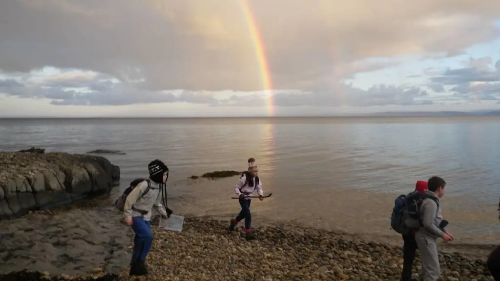 children on a rocky beach with a rainbow in the background.